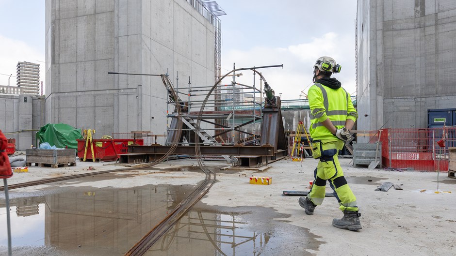 Byggarbetare i gula varselkläder går över arbetsplatsen.