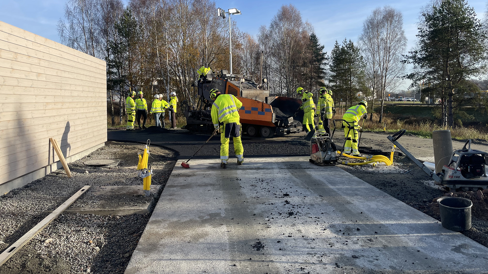 Grupp av yrkesarbetare i gula skyddskläder arbetar med utläggning av Asfalt Zero på handelsplats i Eksjö.