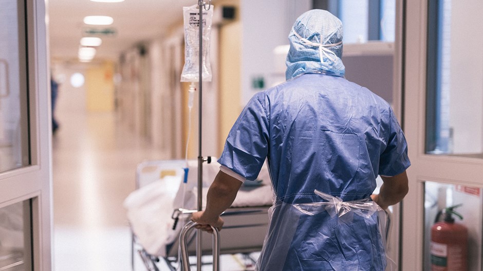 Vårdpersonal rullar en sjukhussäng i en korridor.