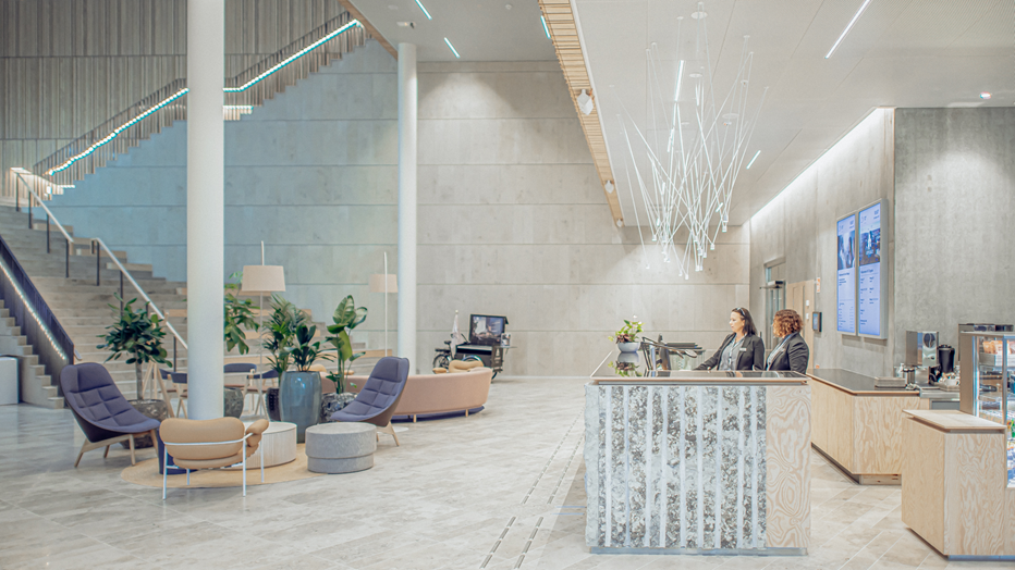 I entréplanet ligger receptionen och intill finns både café och restaurang. Till vänster skymtas den stora trappan, loungedel med fåtöljer och soffa. till höger syns receptionsdisken med två personer och en del av restaurangens diskar.