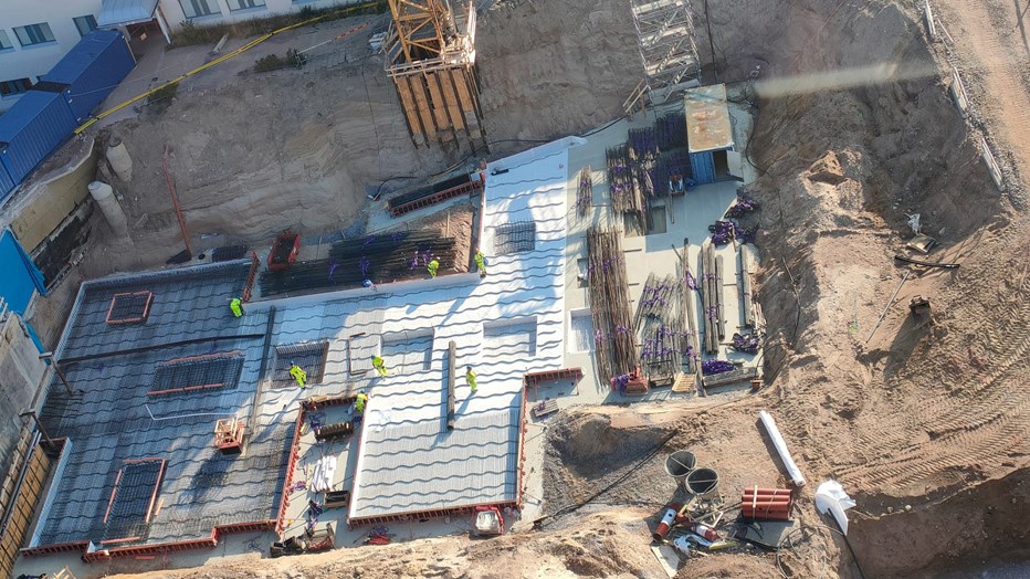 The workplace is cramped and requires elaborate distribution and logistic management.  The construction site from above. Construction workers in yellow clothes at work.