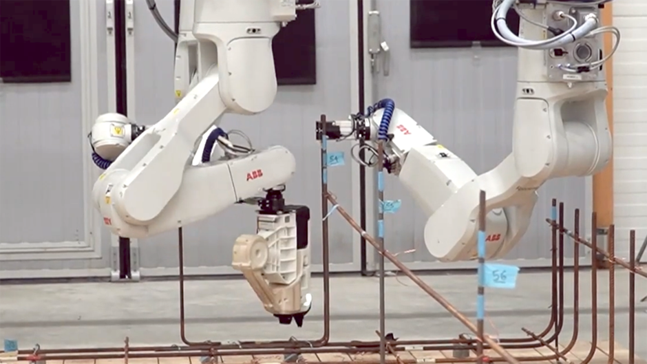 Två robotar jobbar sida vid sida med att bygga en armeringskorg i järn.