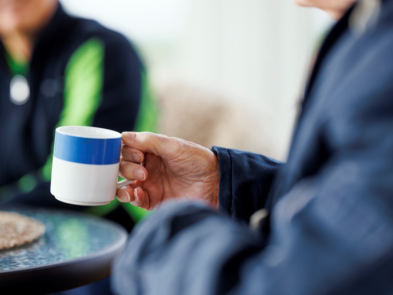 En äldre person som håller i en kaffekopp.