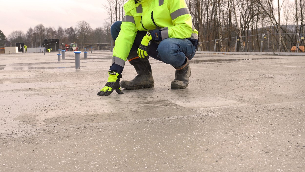 Person i varselkläder sitter på huk med ena handen på en gjuten betongplatta.