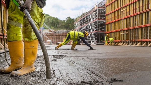 Gjutning av betong i en stor form. En person som man bara ser de gula stövlarna på fyller betong den andra slätar till den.