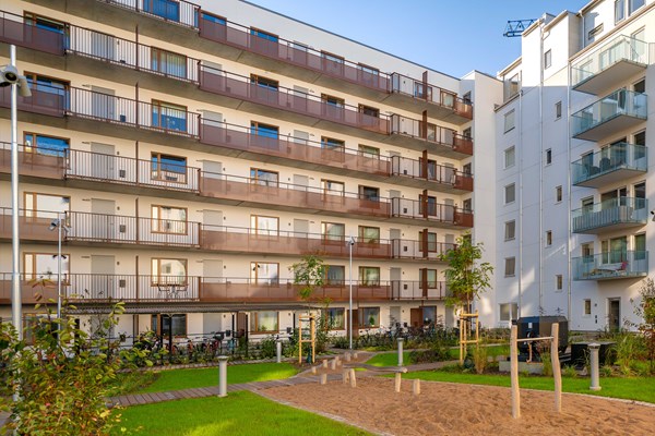 Innergård med lekpark, gräsmatta och träd omringad av bostadshusens fasader.